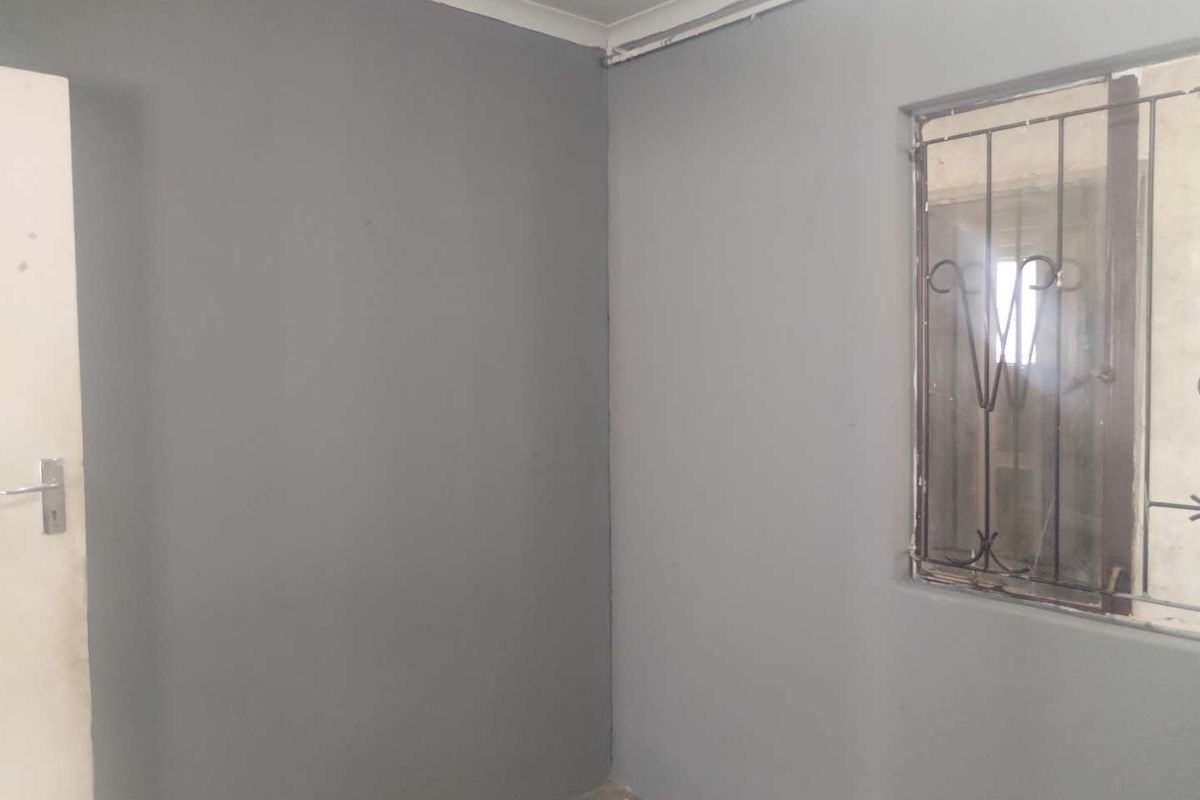 An empty bedroom featuring grey painted walls, a window with a security gate, and exposed surface wiring.