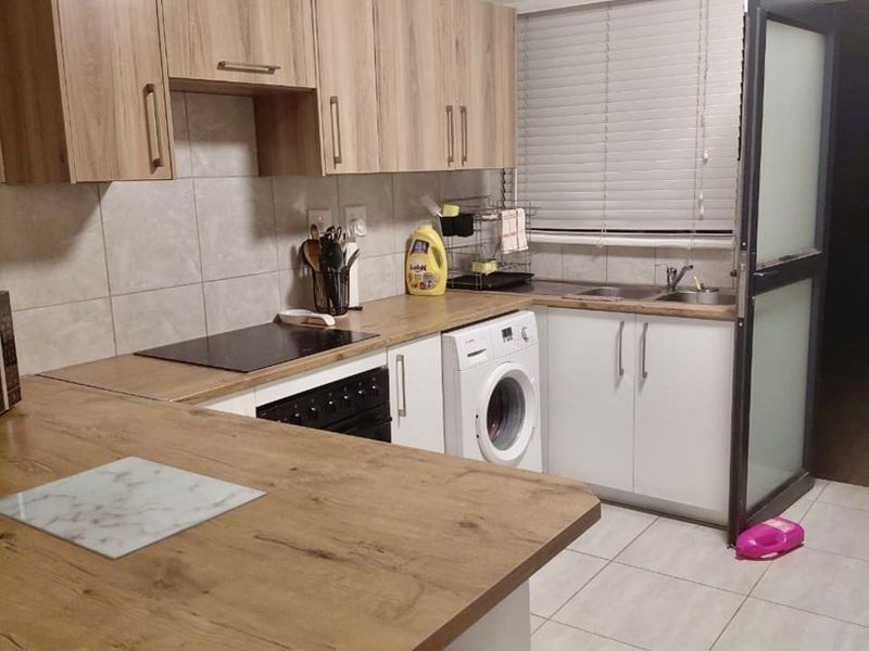 Functional kitchen featuring wood-look laminate countertops, light-toned cabinetry, tiled backsplash, and integrated appliances including a hob and oven.