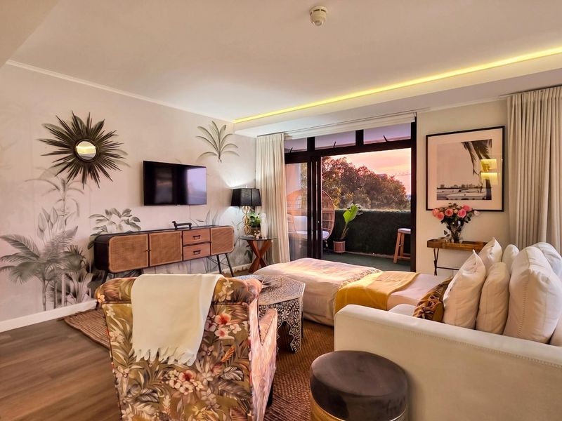 A well-lit living room featuring recessed ceiling lighting, laminate flooring, and large sliding glass doors that open onto a private balcony.