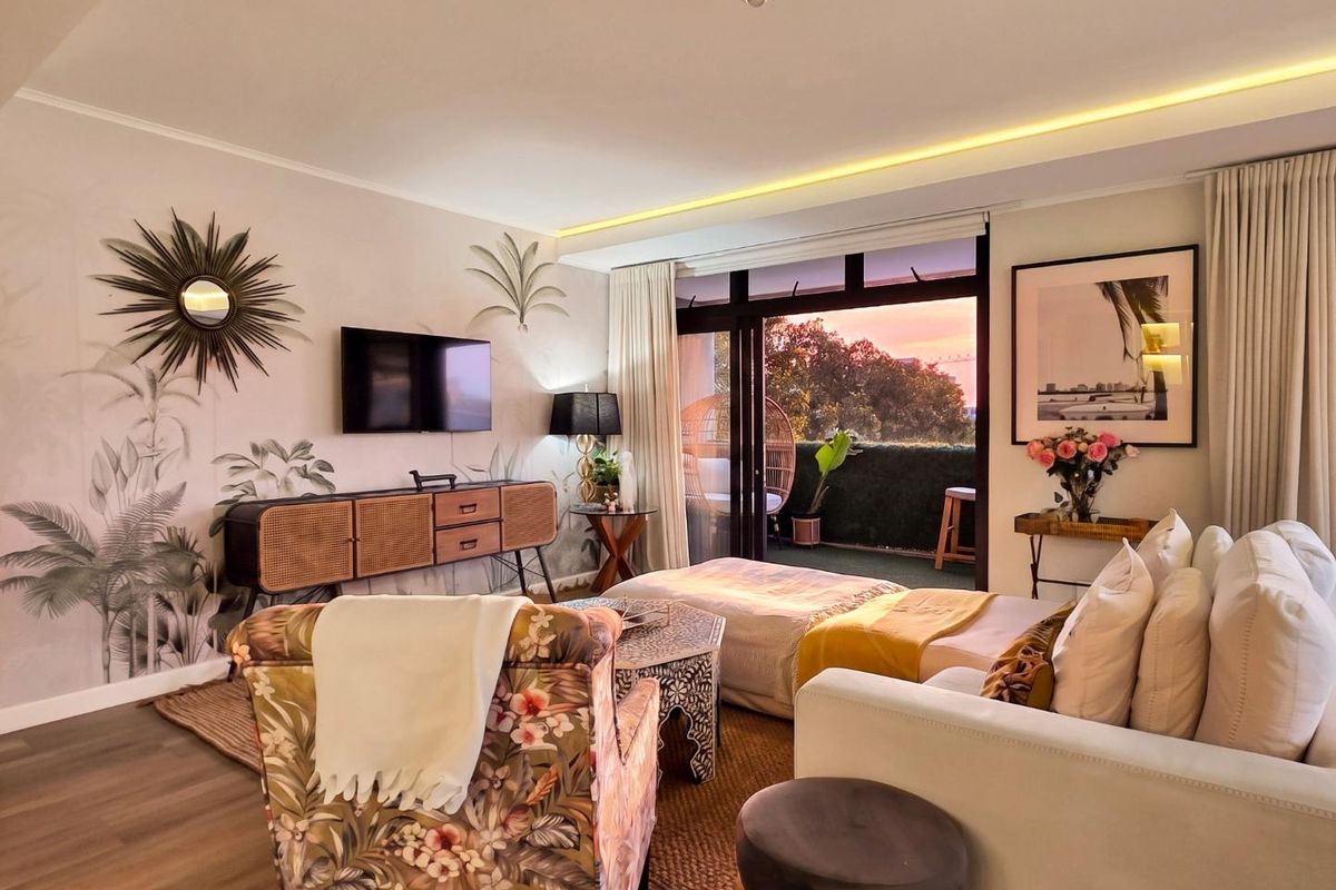 A well-lit living room featuring recessed ceiling lighting, laminate flooring, and large sliding glass doors that open onto a private balcony.
