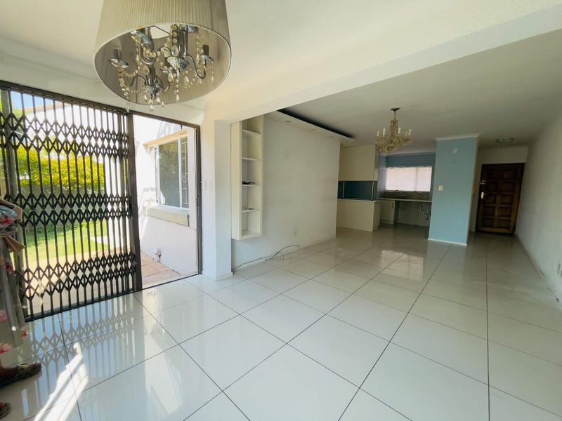 Spacious open-plan living and kitchen area featuring white tiled flooring, built-in shelving, and direct access to the exterior through a security gate.