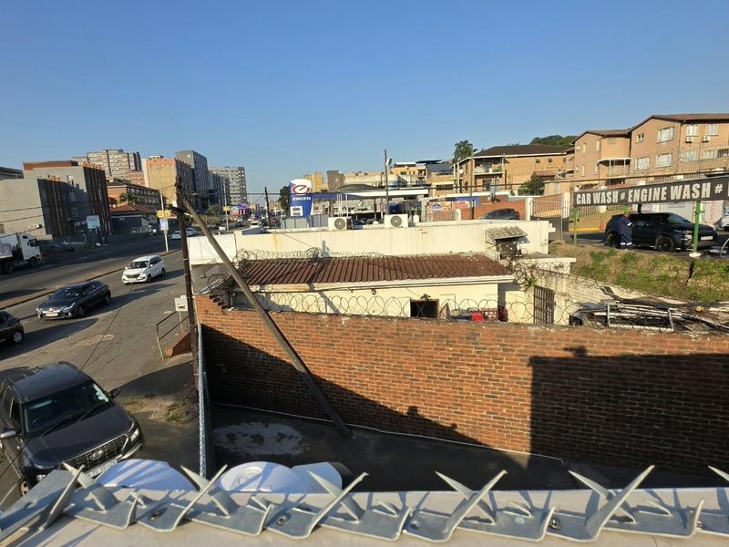 Elevated street view showing a commercial property with a brick boundary wall, razor wire security, and adjacent urban infrastructure.