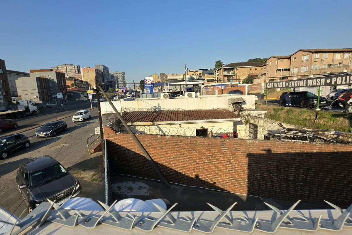 Elevated street view showing a commercial property with a brick boundary wall, razor wire security, and adjacent urban infrastructure.