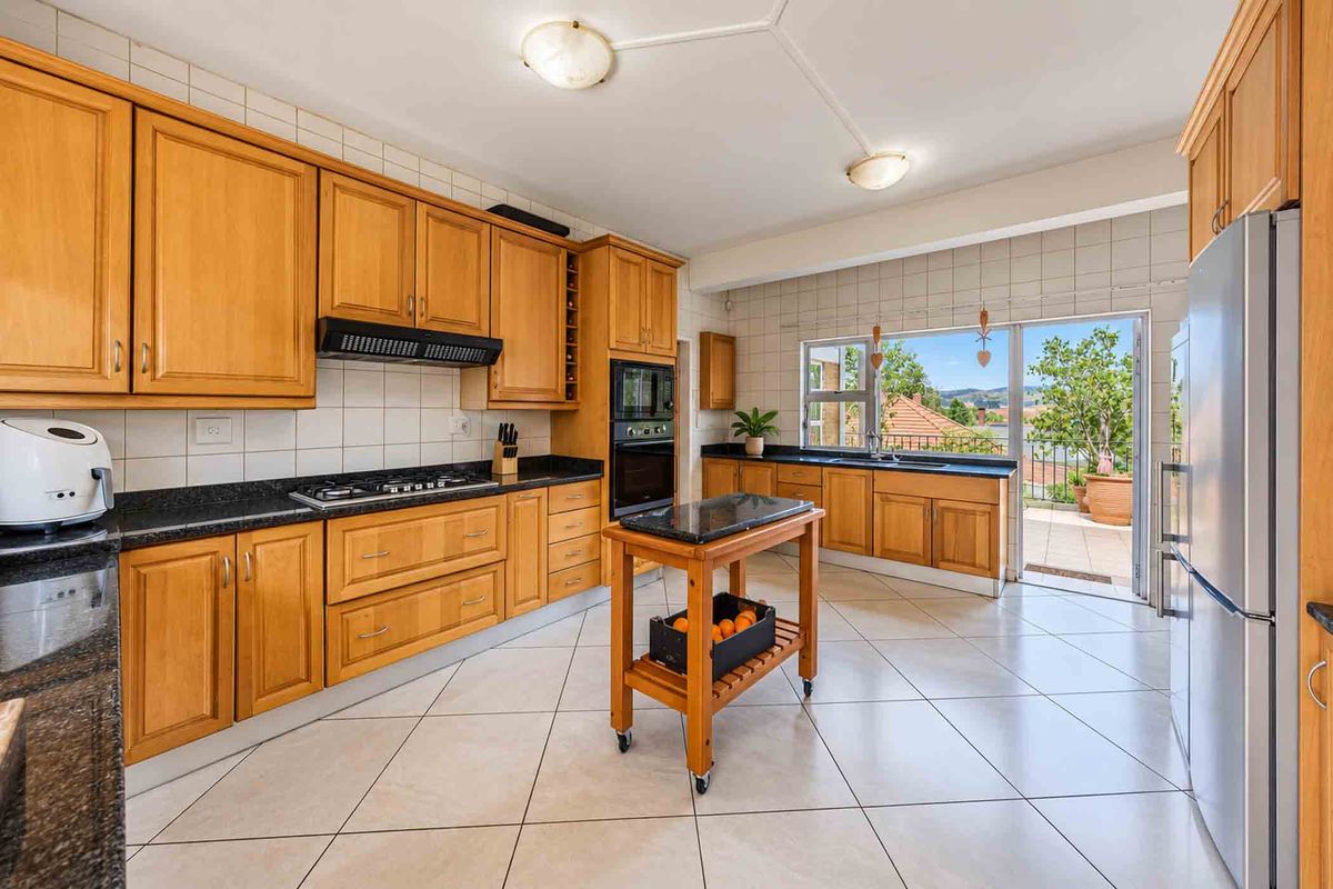 Spacious kitchen featuring wooden cabinetry, granite countertops, built-in oven, gas hob, and direct access to an outdoor patio area.