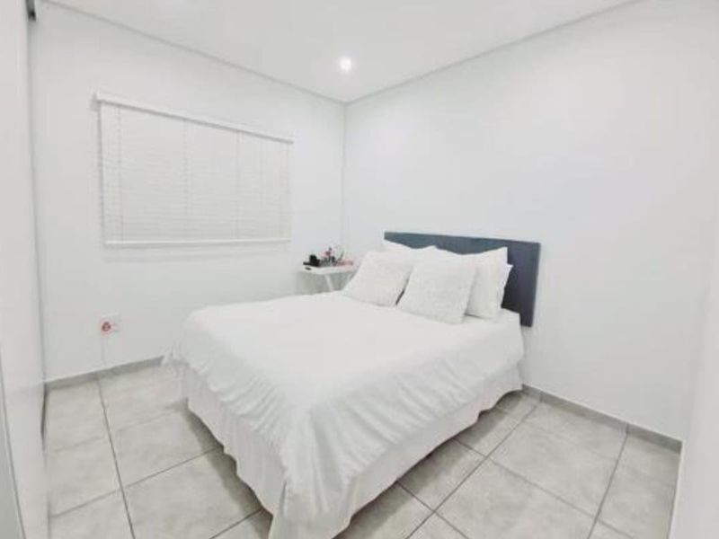 A clean and bright bedroom featuring neutral tiled flooring, recessed lighting, and fitted window blinds.