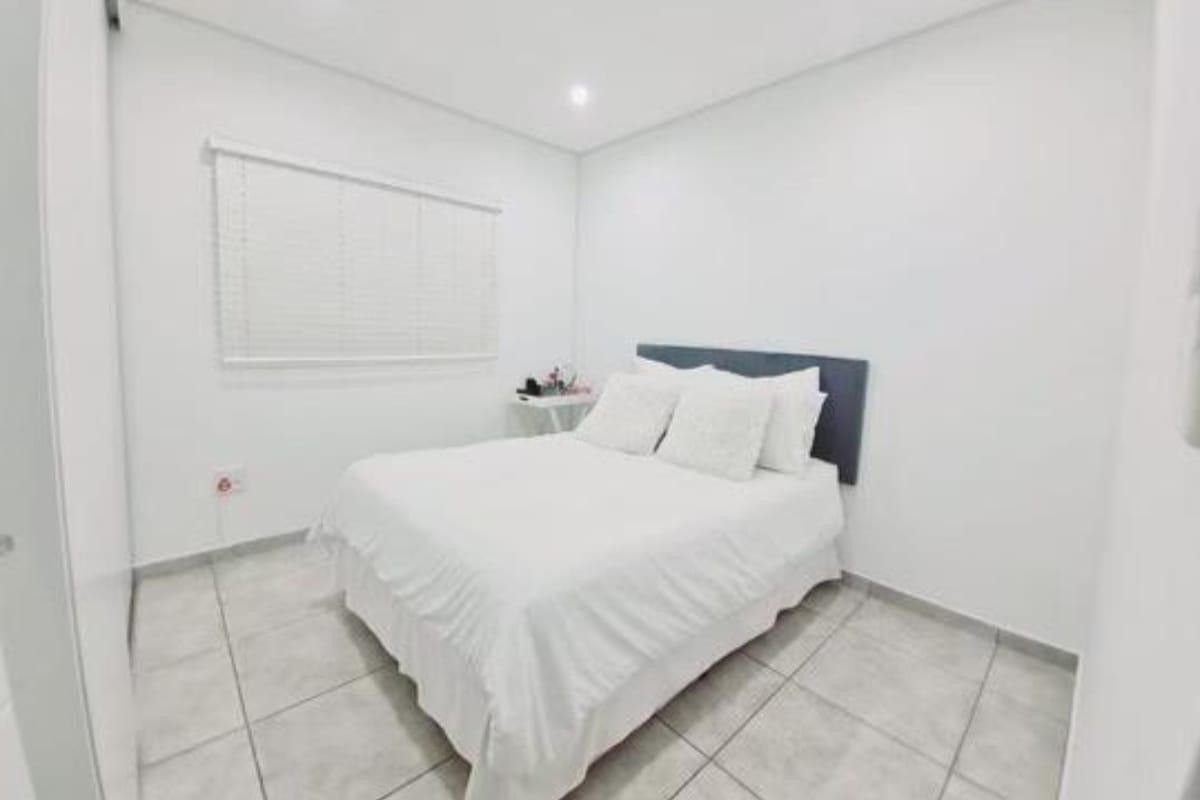 A clean and bright bedroom featuring neutral tiled flooring, recessed lighting, and fitted window blinds.