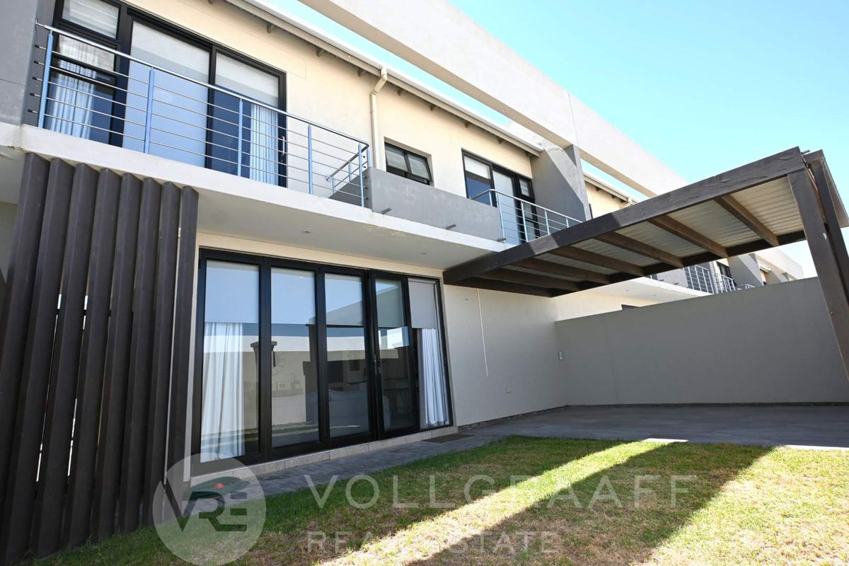 Rear view of the townhouse featuring a paved patio area, a small lawn, and a balcony with stainless steel railings on the upper level.