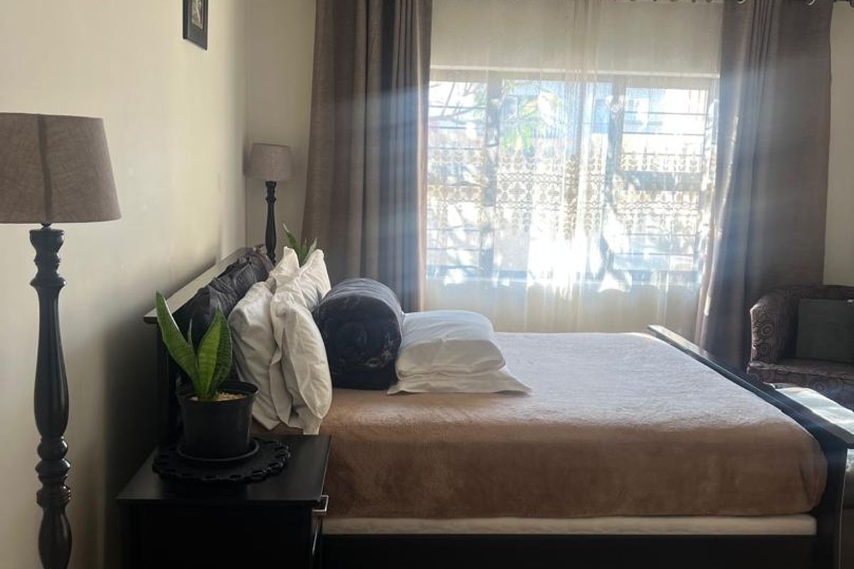 A well-lit bedroom featuring tiled flooring, coved ceilings, and a window fitted with security bars.