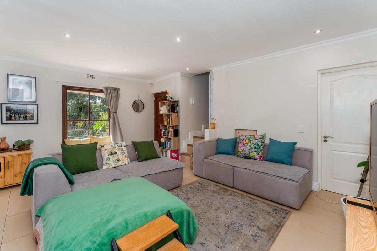 A bright and comfortable living room featuring tiled flooring, recessed downlighting, and a large window with views of the garden.