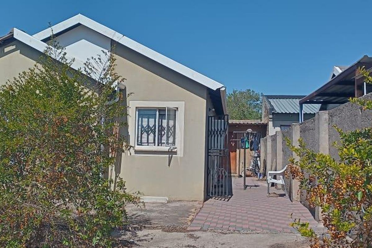 Exterior view of a single-story house featuring a paved side walkway, security gates, and a modest garden area.