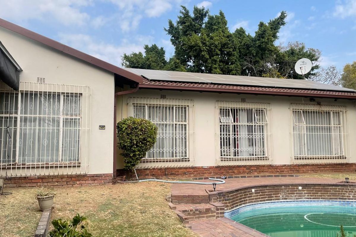 Rear exterior view of the house featuring a swimming pool, brick pool surround, and roof-mounted solar panels with security bars on windows.