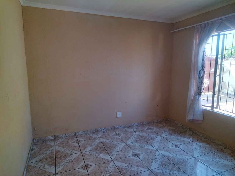 An empty bedroom featuring tiled flooring, security bars on the window, and a curtain rail, ready for personalization.