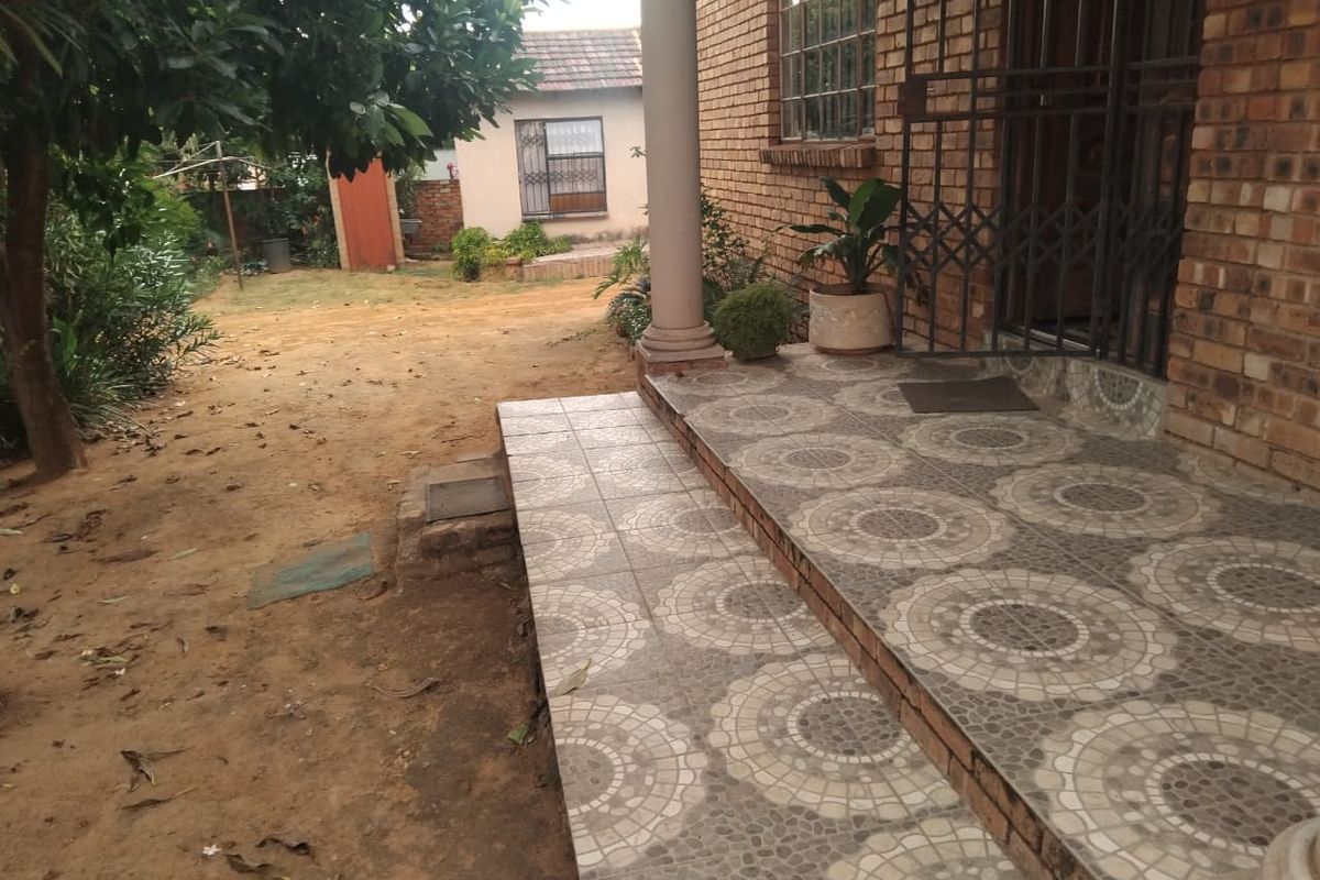 A rear exterior view featuring a tiled patio area, brick facade, and a garden space with established trees.