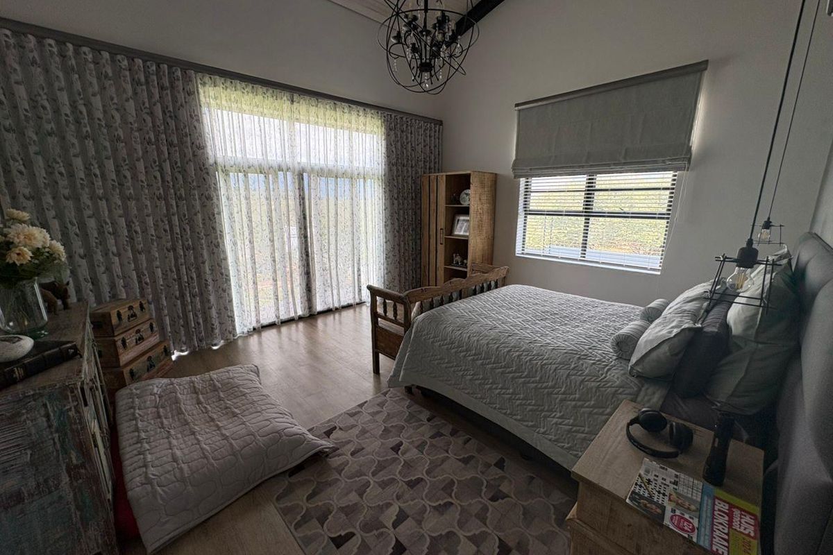 A well-lit bedroom featuring high vaulted ceilings, large sliding glass doors with floor-to-ceiling curtains, and modern laminate flooring.