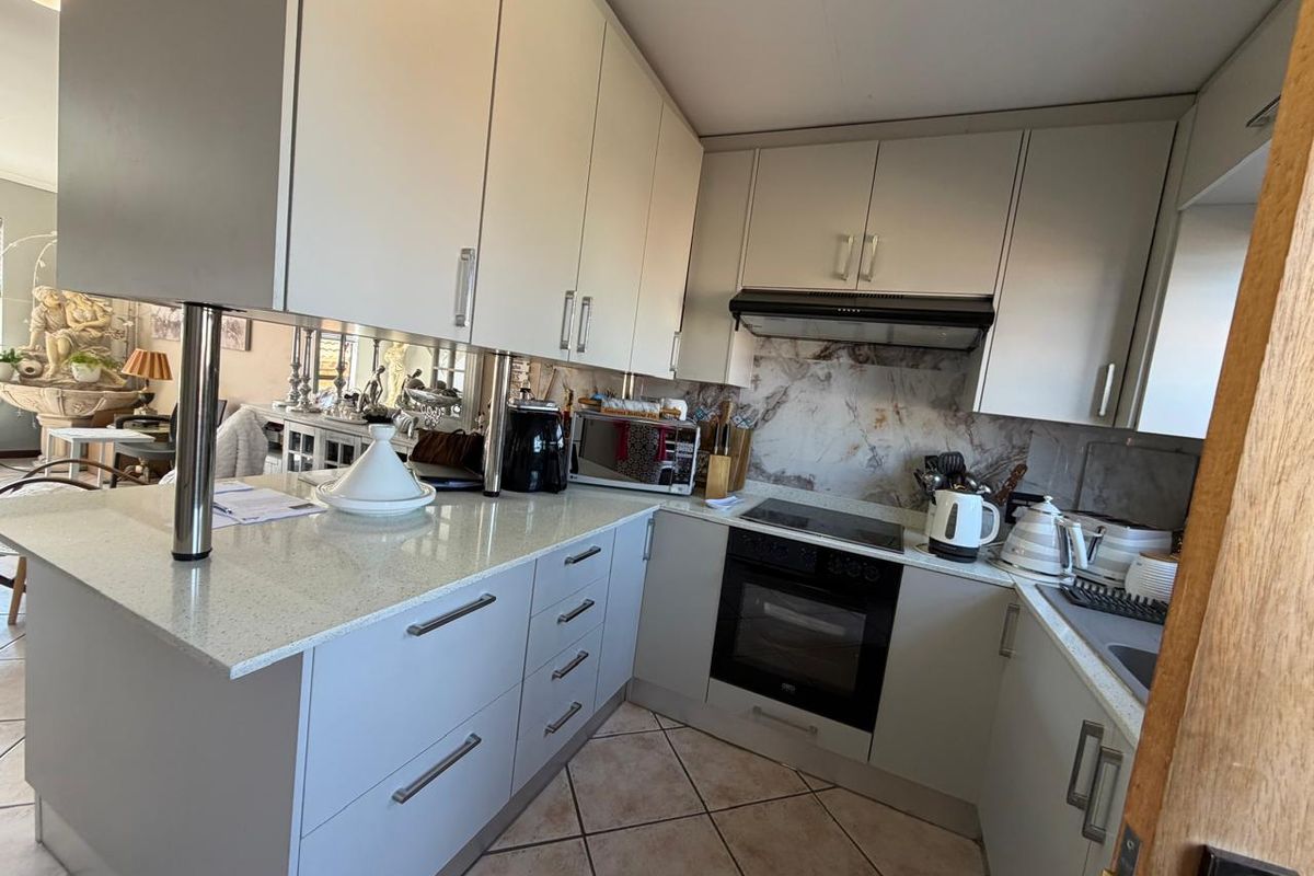 Modern kitchen featuring light-toned cabinetry, stone countertops, integrated oven and hob, and a stylish mirrored splashback, offering a functional and clean workspace.