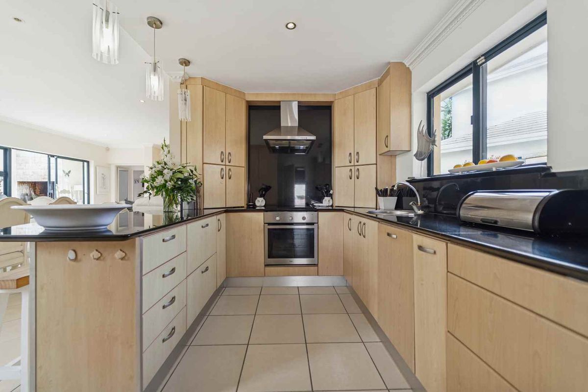 A well-maintained kitchen featuring light wood cabinetry, black granite countertops, stainless steel appliances, and ceramic tile flooring with integrated lighting.