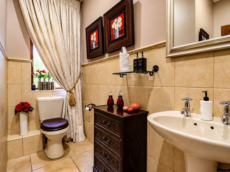 A well-maintained guest bathroom featuring neutral ceramic wall and floor tiling, a pedestal basin with classic fixtures, and a standard toilet.