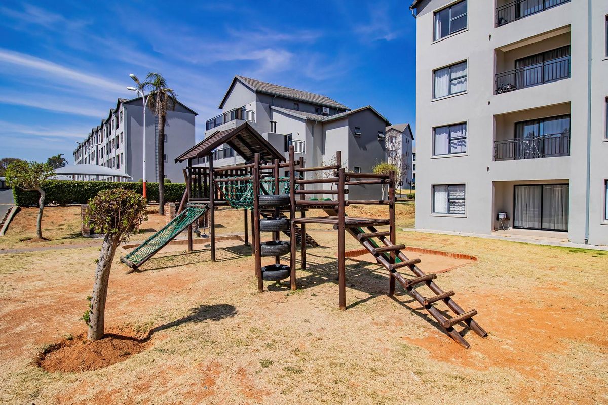 Exterior view of an apartment complex featuring a communal playground area with wooden climbing structures and landscaped grounds.