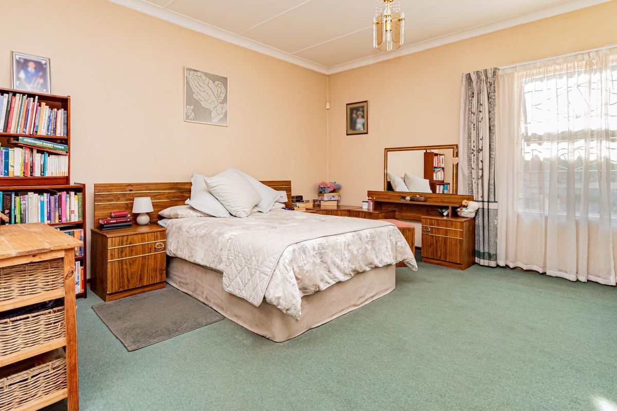 Spacious bedroom featuring built-in wooden cabinetry, a vanity unit, and large windows with curtain rails, offering a functional and well-lit living space.