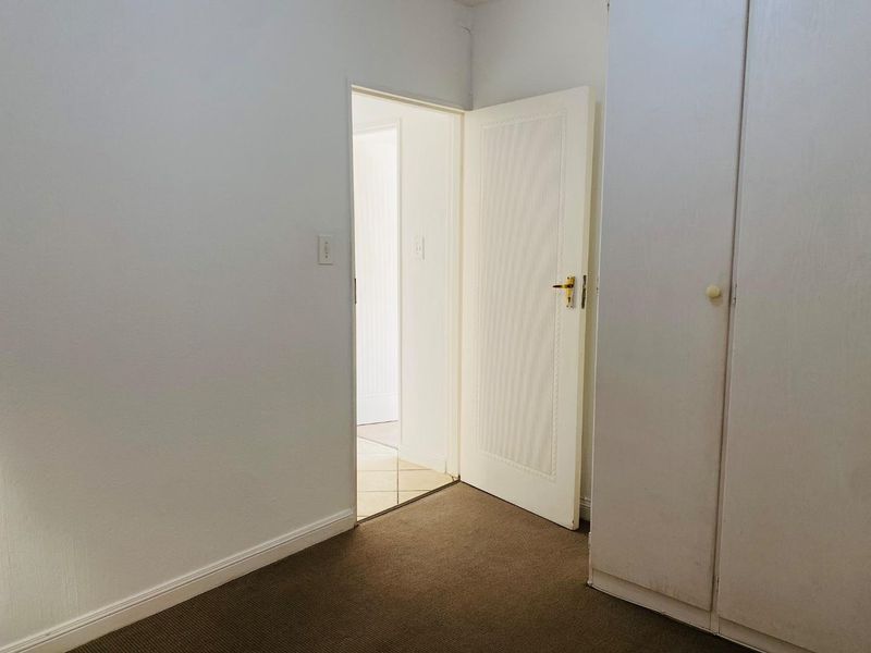 An empty bedroom featuring neutral walls, carpet flooring, and a built-in wardrobe, with an open doorway leading to an adjacent hallway.