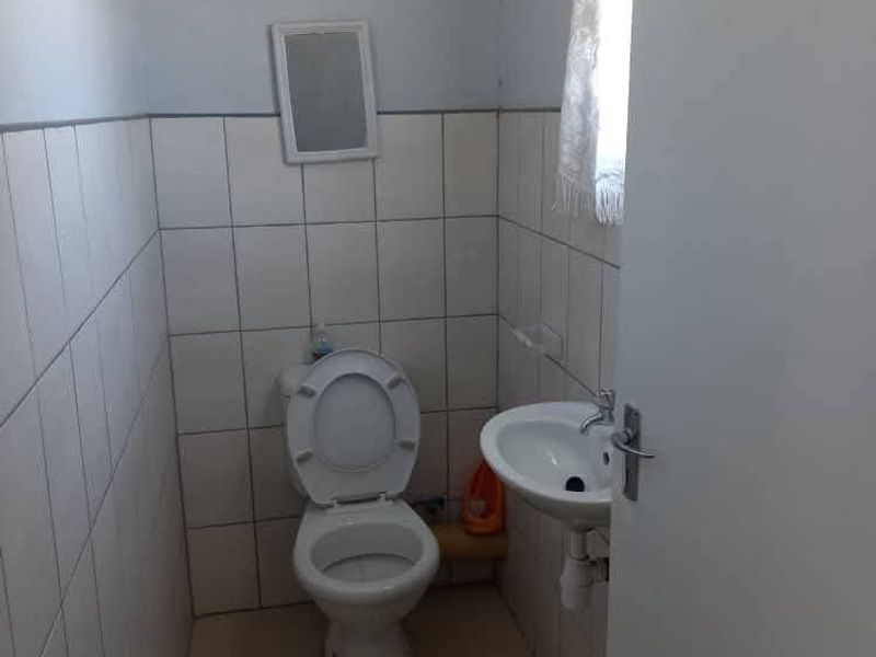 A compact bathroom featuring a standard ceramic toilet and a wall-mounted basin with tiled walls and flooring.