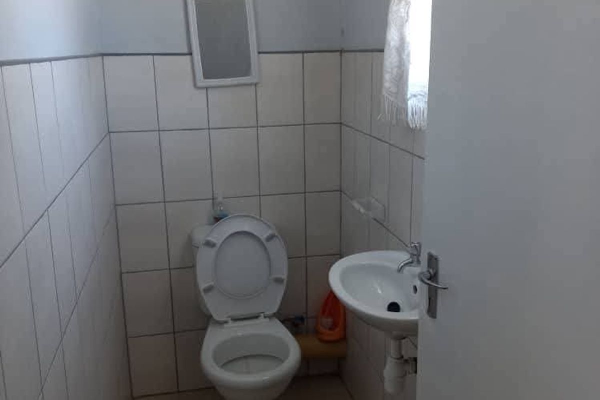 A compact bathroom featuring a standard ceramic toilet and a wall-mounted basin with tiled walls and flooring.