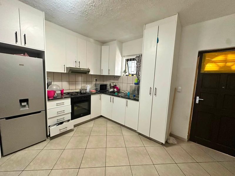 A functional kitchen featuring white built-in cabinetry, a tiled backsplash, integrated oven and hob, and tiled flooring.