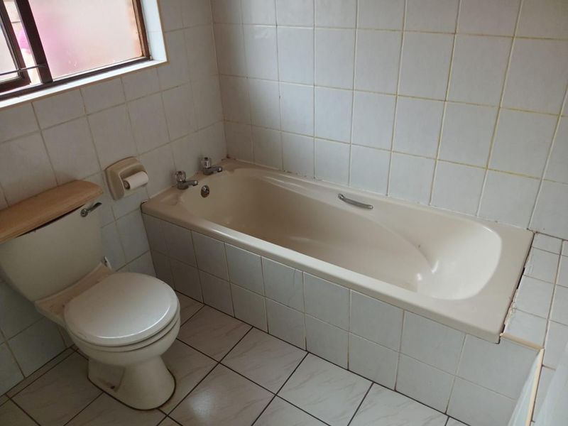 A dated bathroom featuring a standard bathtub, toilet, and white ceramic wall and floor tiling, offering potential for a modern renovation.