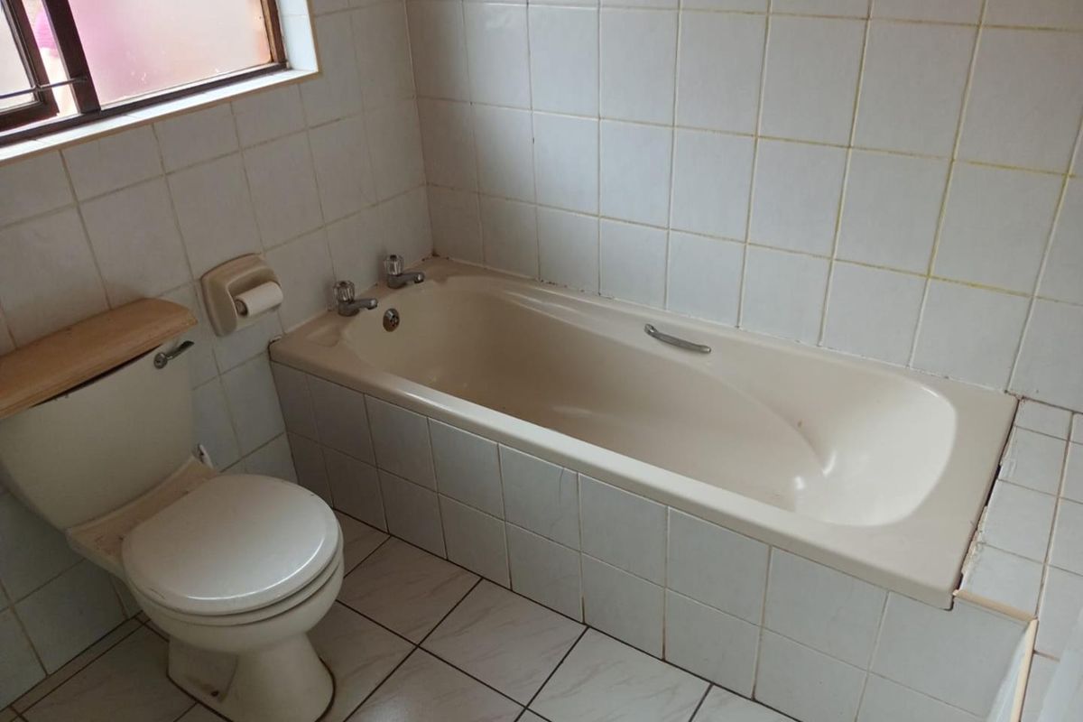 A dated bathroom featuring a standard bathtub, toilet, and white ceramic wall and floor tiling, offering potential for a modern renovation.