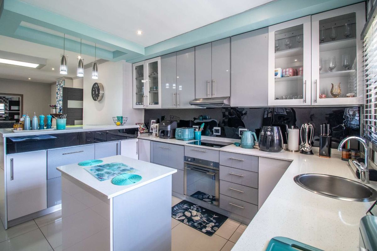 Modern kitchen featuring sleek grey cabinetry, white stone countertops, a central island, integrated oven, and a black glass splashback.