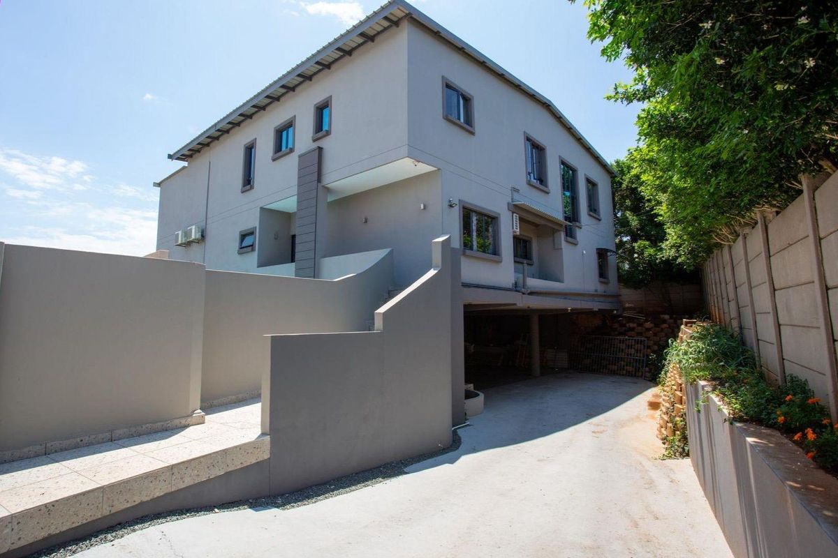 A view of the exterior rear of the multi-story house, featuring a paved driveway, retaining walls, and modern architectural design.