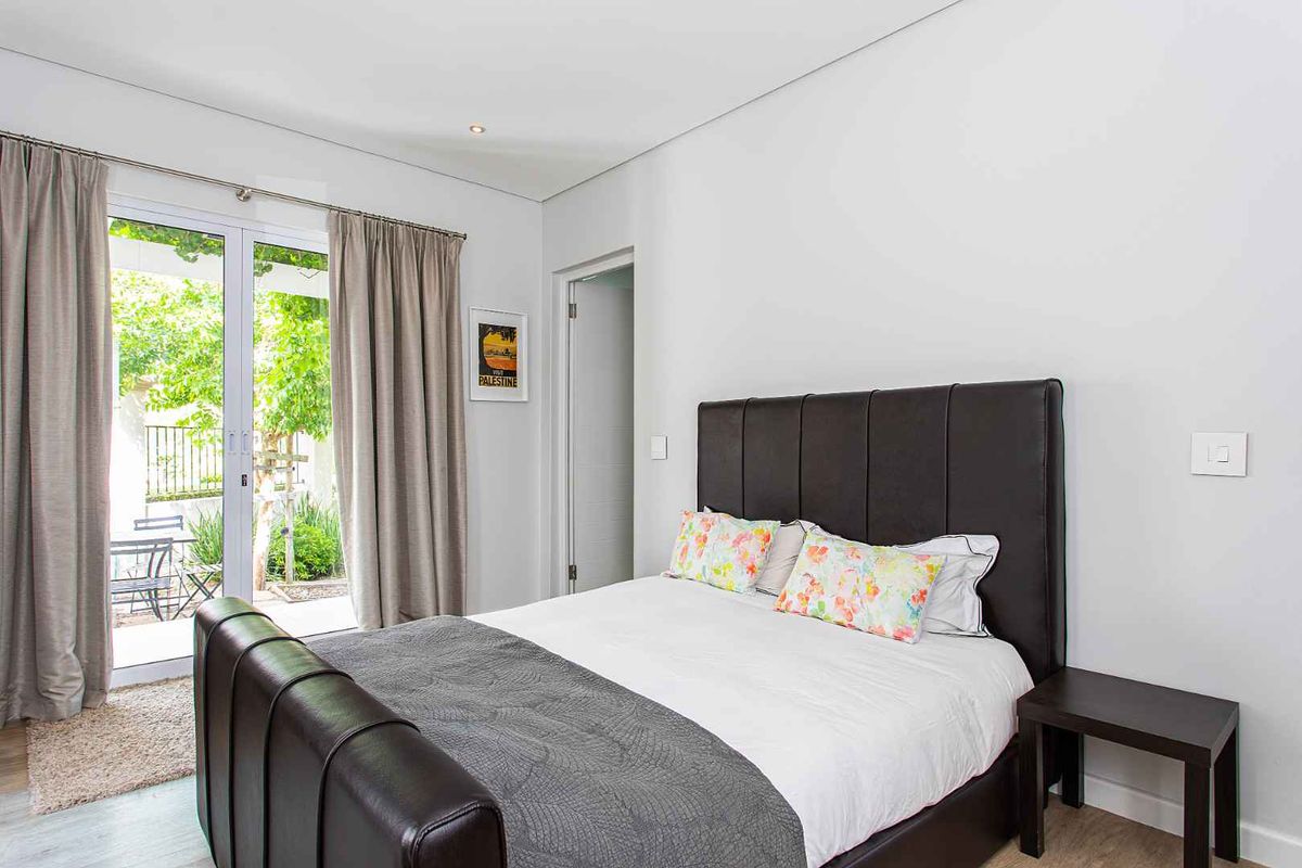 A bright bedroom featuring modern laminate flooring, recessed lighting, and a sliding glass door providing direct access to the outdoor patio area.