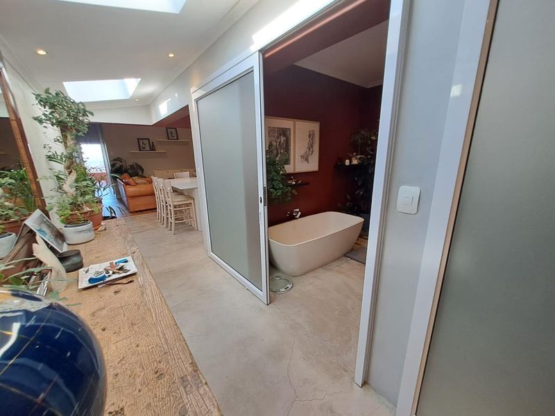 A view from a hallway into an open-plan living area and a modern bathroom featuring a freestanding bathtub and sliding glass door.