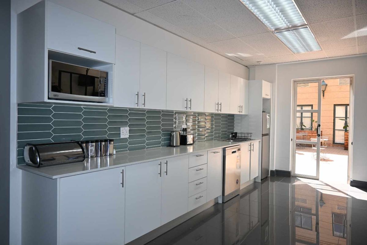 Modern office kitchen featuring white cabinetry, quartz countertops, a stylish tiled backsplash, and integrated appliances, with direct access to an outdoor patio area.