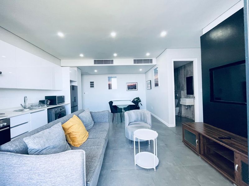 Modern open-plan living area featuring a sleek white kitchen, tiled floors, ducted air conditioning, and a striking black feature wall with integrated television space.