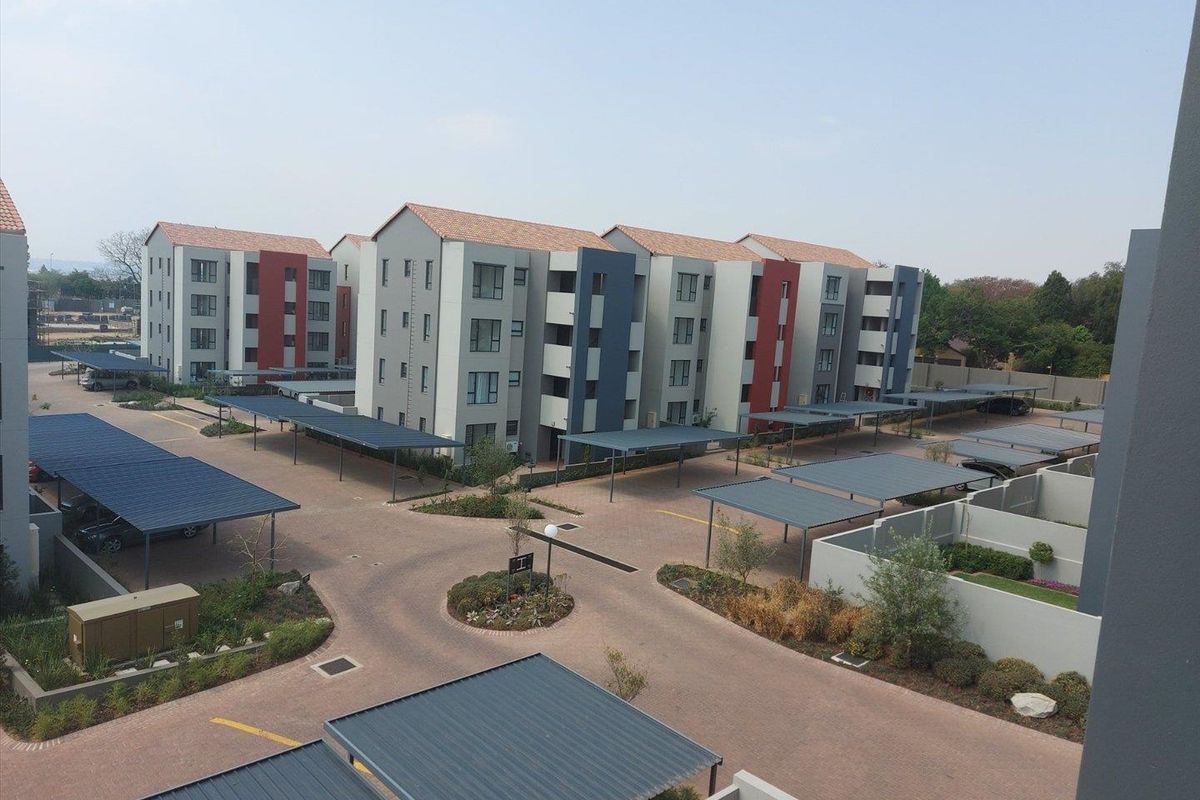 An elevated view of a modern apartment complex featuring paved driveways, covered parking carports, and landscaped communal garden areas.