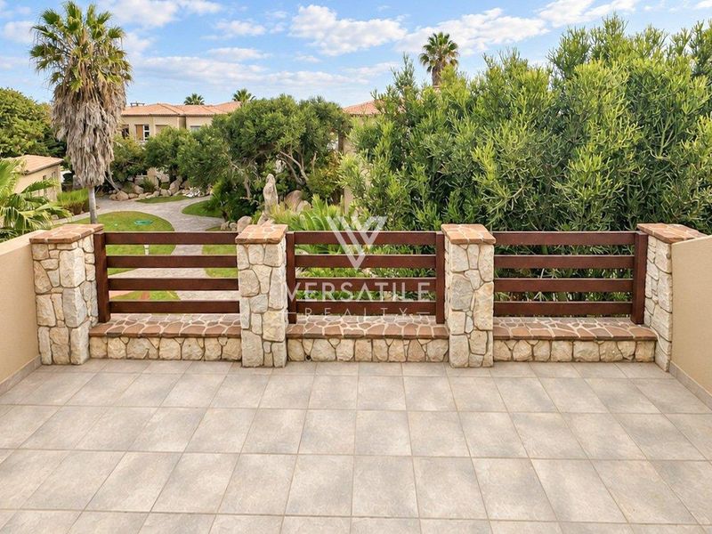 A spacious balcony featuring stone-clad pillars, timber slat balustrades, and tiled flooring, offering a pleasant view of the surrounding estate gardens.