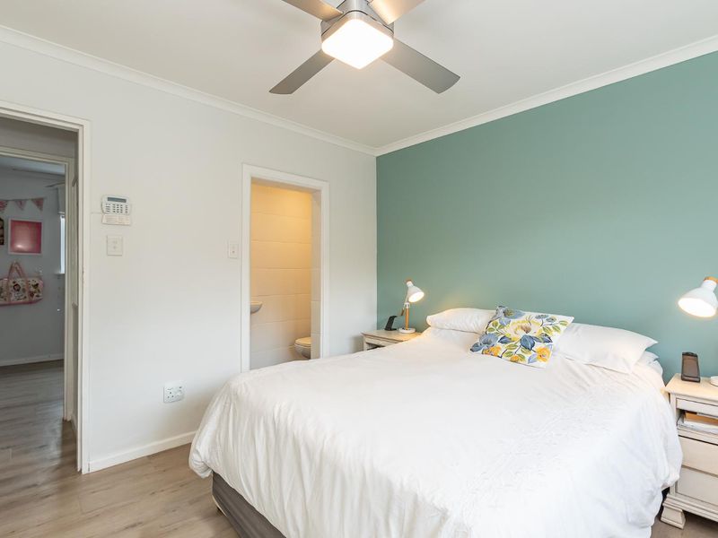 A well-maintained bedroom featuring laminate flooring, a ceiling fan, and an adjoining en-suite bathroom with a feature wall.