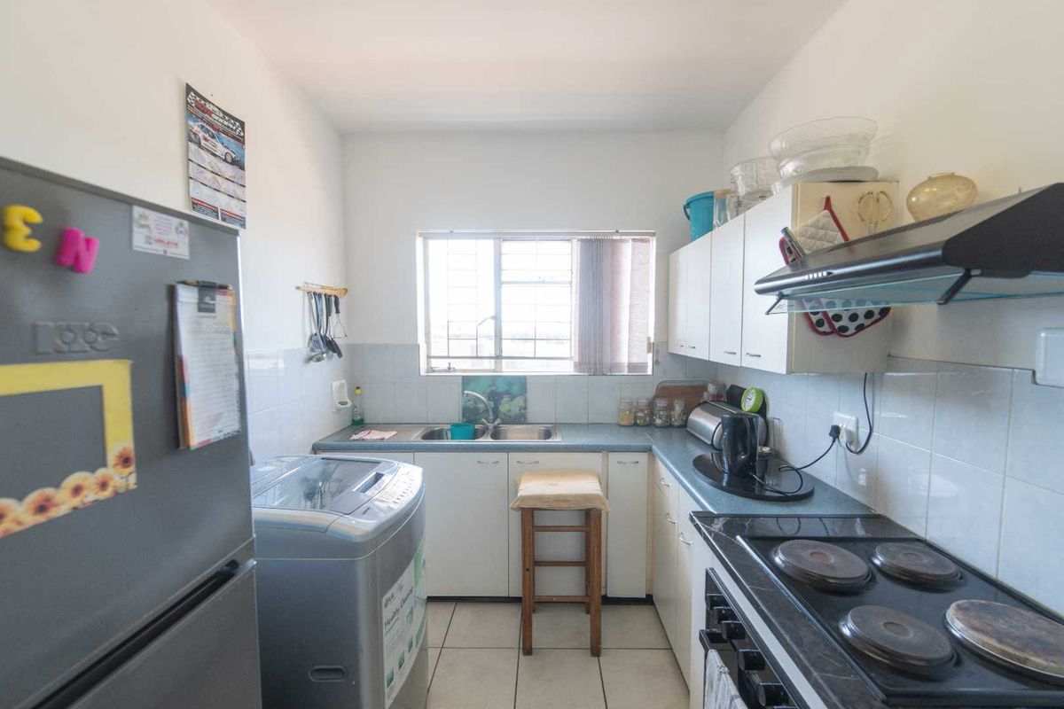 A functional kitchen featuring built-in cabinetry, a double sink, a built-in stove with extractor fan, and tiled flooring with space for laundry appliances.