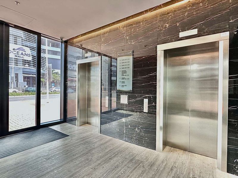 Modern office building lobby featuring polished dark marble wall cladding, stainless steel elevator doors, and large glass entrance doors.