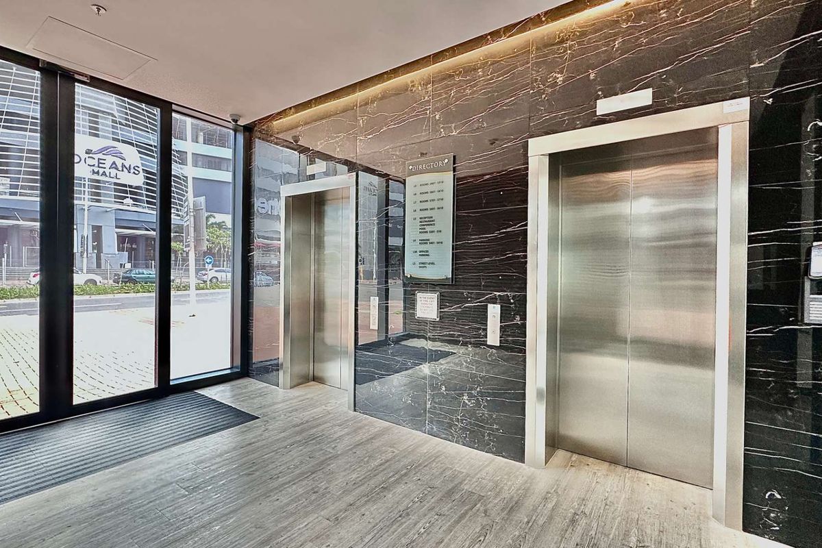 Modern office building lobby featuring polished dark marble wall cladding, stainless steel elevator doors, and large glass entrance doors.