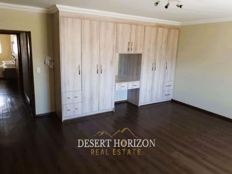 Spacious bedroom featuring extensive light wood-finish built-in cupboards with an integrated vanity area and dark laminate flooring.