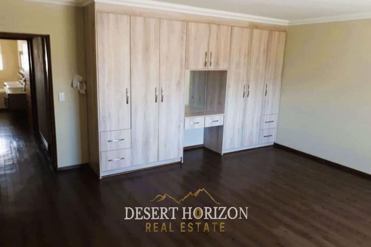 Spacious bedroom featuring extensive light wood-finish built-in cupboards with an integrated vanity area and dark laminate flooring.
