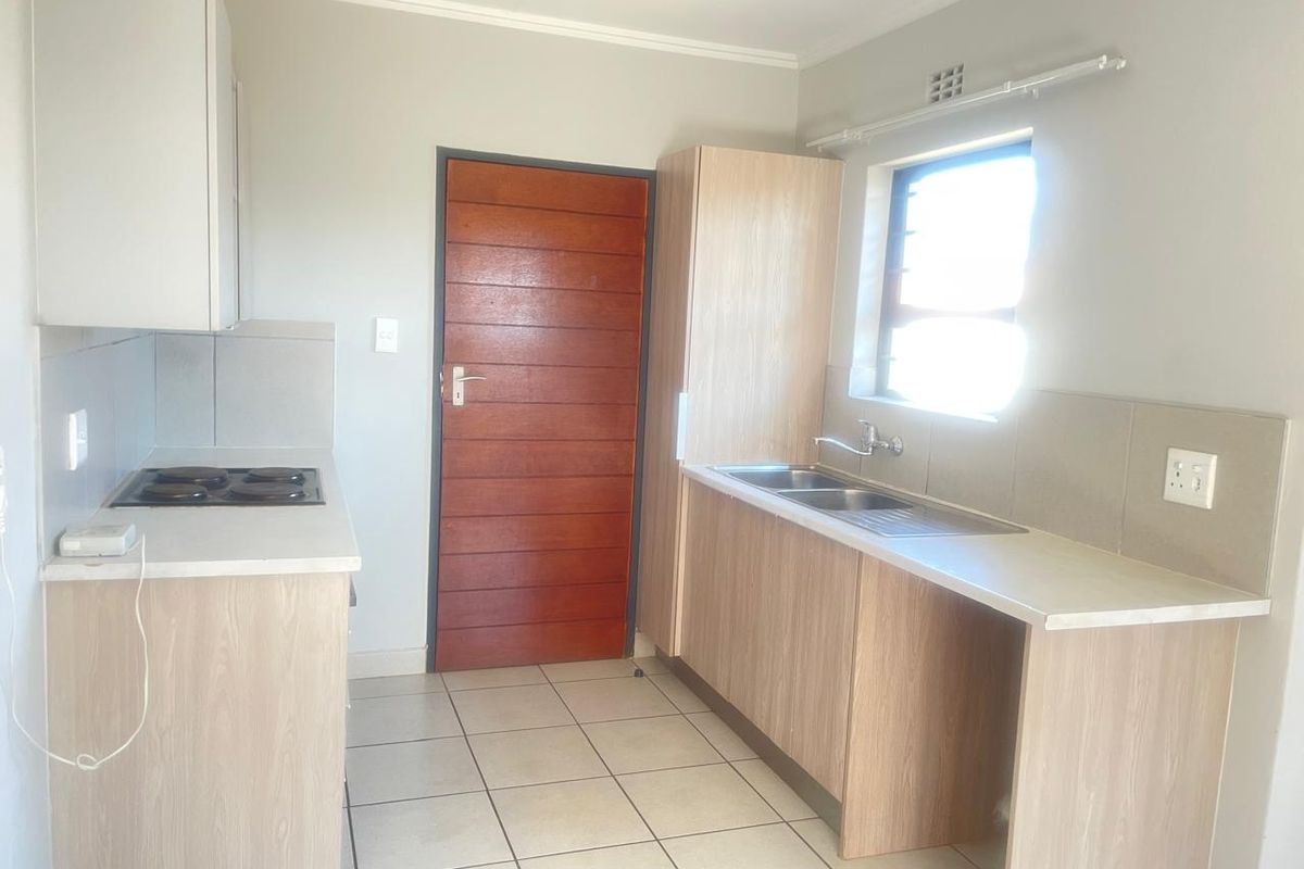 A functional kitchen featuring light wood-look cabinetry, laminate countertops, an electric hob, and a double sink with tiled splashbacks and flooring.