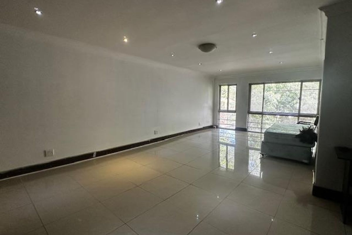 A spacious, open-plan living area featuring large format floor tiles, recessed downlighting, and expansive windows providing natural light.