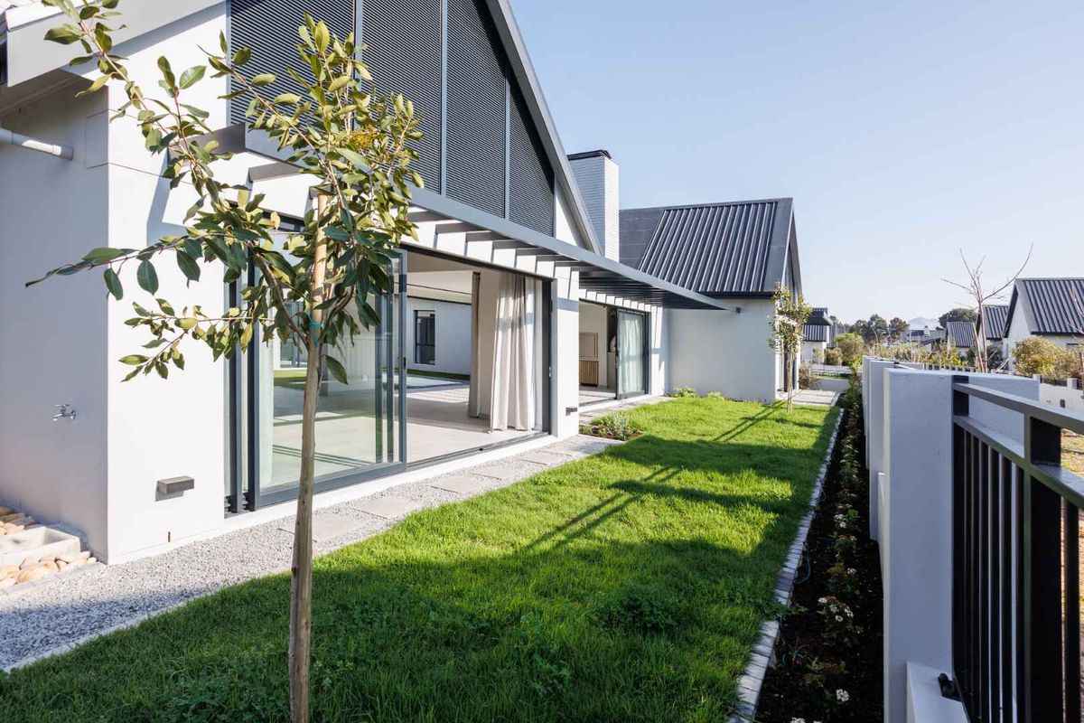 A modern rear exterior view featuring a well-maintained lawn, sliding glass doors, and contemporary architectural finishes with a metal roof.