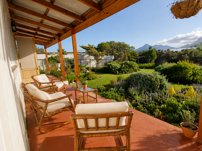 A covered outdoor patio featuring a timber pergola structure, overlooking a well-maintained garden with mountain views.
