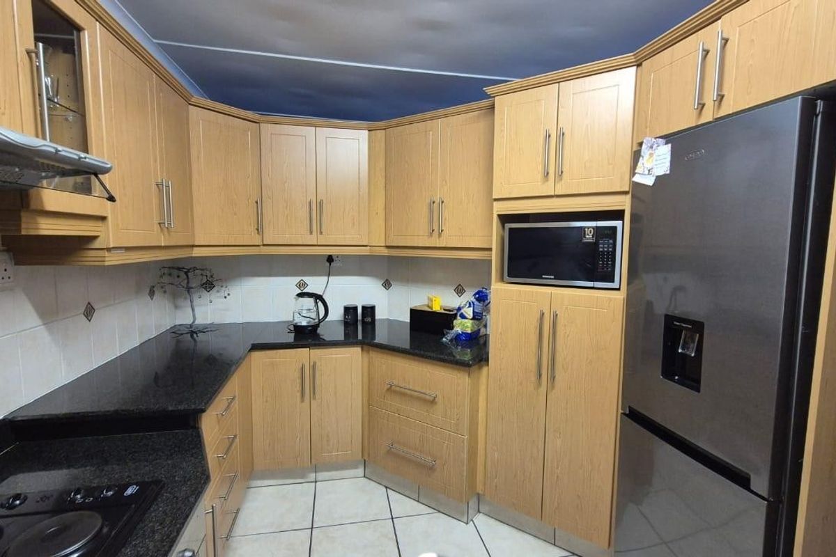 A functional kitchen featuring light wood-finish cabinetry, dark granite countertops, tiled backsplash, and built-in appliances including a microwave and extractor fan.