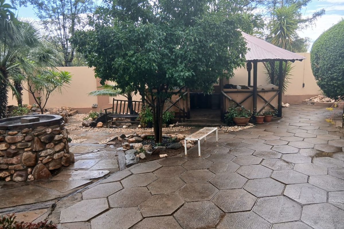 A landscaped rear garden featuring a stone-clad water feature, hexagonal paved patio area, and a covered timber gazebo structure.