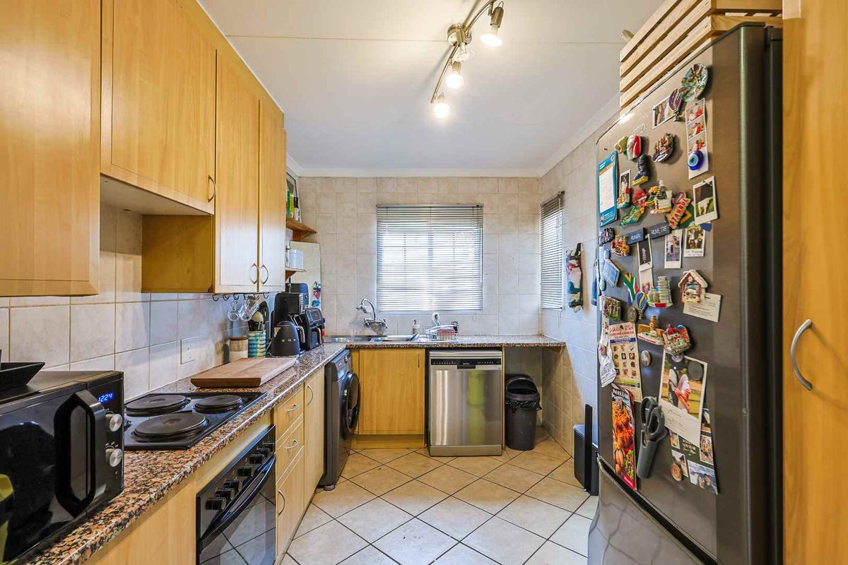 A functional kitchen featuring light wood cabinetry, granite countertops, tiled flooring, and integrated space for laundry appliances.
